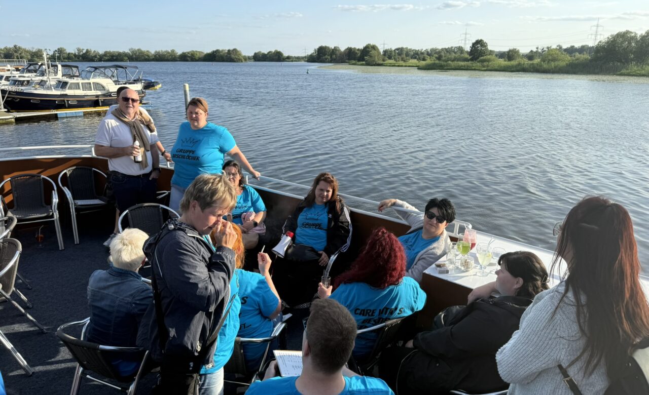 Personen auf dem Boot am sitzen am Tisch und einige stehen mit einem Getränk in der Hand