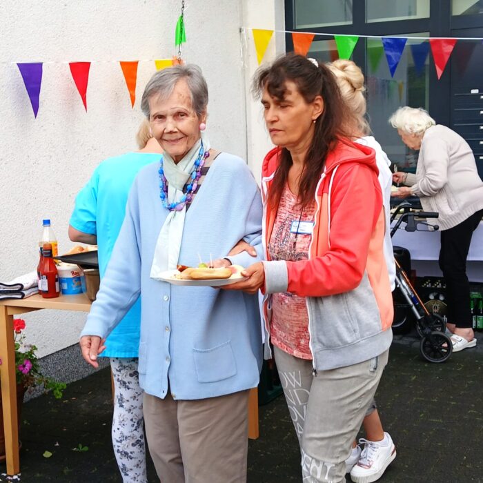 Eine ältere Dame wird mit dem Essen zum Tisch begleitet
